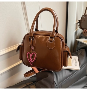 Detailed shot of brown glossy leather Boston bag with heart charm and side pockets