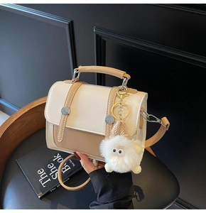 Detail of a beige mini crossbody bag with plush charm on a vintage wooden chair