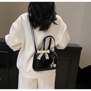 Detail of black patent leather Boston bag with lace bow and silver bear charm