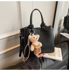 Detail of black lychee grain tote bag with adjustable strap and cute teddy bear charm