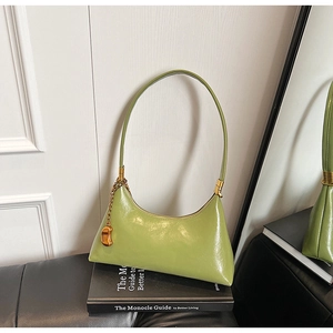 Detail der hellgrünen glänzenden Hobo-Tasche mit goldenem Anhänger auf einem Buch