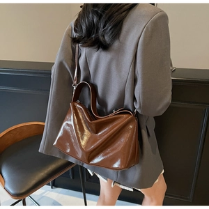 Rear view of a shiny brown patent leather crossbody bag on a grey suit jacket
