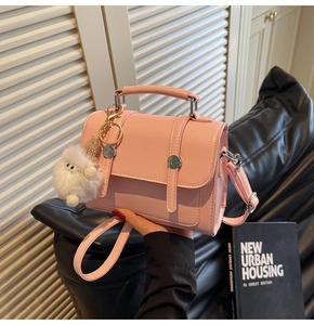 Pink minimalist handbag with metal buckle and plush charm detail in hand