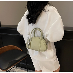 Gros plan du sac Boston en cuir grainé vert clair avec breloque cœur et bandoulière amovible