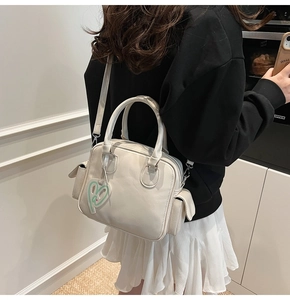 Detail of white textured leather Boston bag featuring side pockets and heart charm accessory