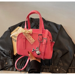 Detail of a bright pink patent leather Boston bag with lace bow and silver dog charm