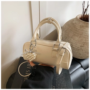 Détail du sac crème présentant une texture en cuir plissé et un charme cœur en perle