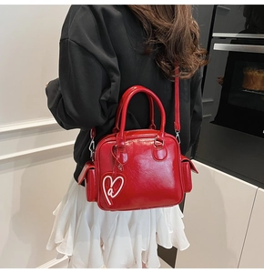 Close-up of a red glossy Boston tote bag with side pockets and a heart-shaped charm