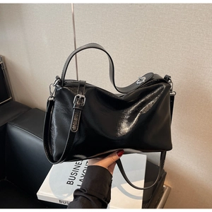 Detail of glossy black patent leather pillow bag with silver metal lock and top handle
