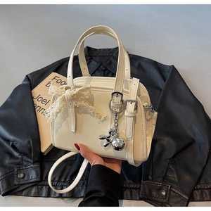 Close-up of cream white Boston bag with lace bow and silver balloon dog pendant