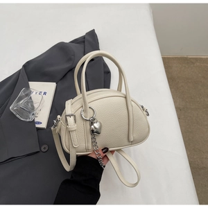 Détail du sac polochon blanc crème montrant le cuir grainé et le pendentif cœur