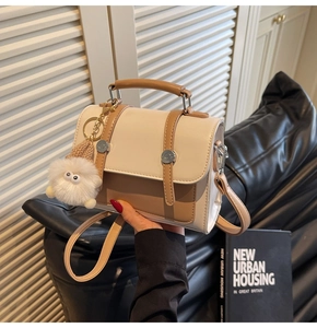 Detail of the chic beige and brown handbag with a white plush charm and top handle
