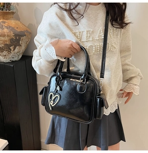 Detail of black glossy PU leather Boston bag featuring side pockets and a heart charm