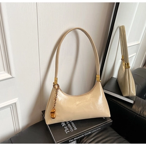 Detail der beigen glänzenden Hobo-Tasche mit Goldkette und bohnenförmigem Metallanhänger