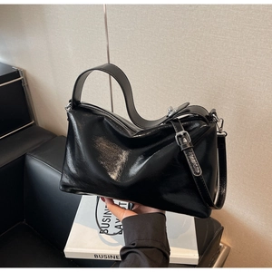 Close-up of black glossy leather handbag with soft pleated texture and silver zipper