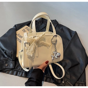Detail of off-white Boston bag featuring lace bow and silver dog charm accessory