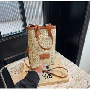 Detailed close-up of straw woven phone bag with brown leather trim and fashion tag