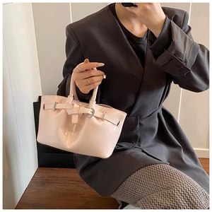 Detailed view of light pink patent leather bucket bag with silver buckle and belt feature