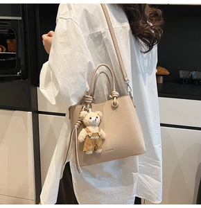 Detail of beige pebble leather bucket bag with top handles and a cute bear charm pendant
