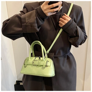 Close-up of bright green shell crossbody bag with metal buckle straps on a model