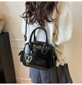 Detail of black glossy Boston bag with heart pendants and functional side pockets