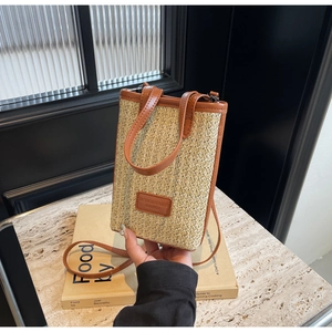 Detailed view of woven straw bucket bag with brown PU leather trim and logo patch