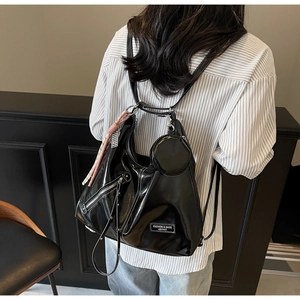 Detail of black glossy leather tote bag with silver zippers and pink ribbon charm accessory