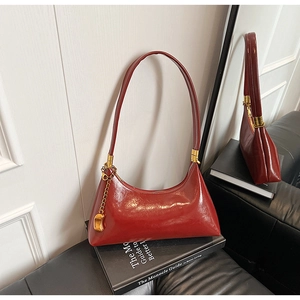 Nahaufnahme der rotbraunen Glanzledertasche mit Gold-Details und Bohnenanhänger