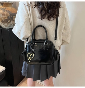 Detail of glossy black Boston bag featuring dual handles and a heart charm pendant