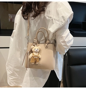 Detail of beige lychee textured bucket bag with cute bear pendant and knotted handle