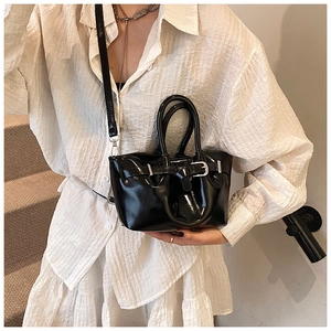 Detail of black patent leather bucket bag with glossy finish and silver buckle strap