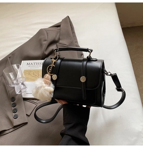 Detail of black leather handbag with silver rings and plush charm on a white surface