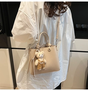 Detail of apricot bucket bag with lychee texture and cute bear pendant on shoulder strap