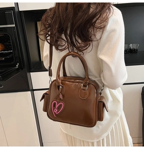Brown glossy leather Boston bag with a pink heart charm shown on a shoulder strap