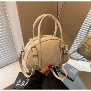 Vue détaillée du cuir grainé blanc cassé et du pendentif cœur sur le sac Boston
