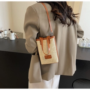 Detail of straw woven crossbody bucket bag with brown leather trim on a stylish model