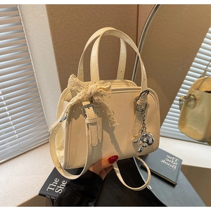 Detail view of cream Boston bag with delicate lace bow and silver bear charm accessory
