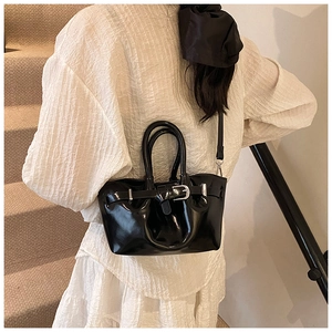 Close-up of a black glossy bucket bag with a metal buckle and shoulder strap worn by a model