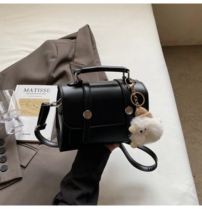 Detailed view of a black PU leather satchel with a white plush lamb charm on a minimalist desk