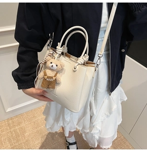 Close-up of white lychee pattern bucket bag with cute bear charm and leather handles