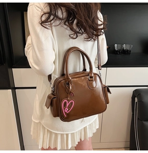 Dark brown patent leather Boston bag with pink heart charm shown on model shoulder