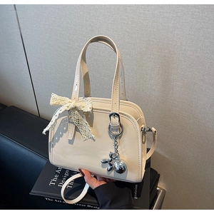 Detail of glossy beige Boston bag featuring lace bow and silver dog charm on book prop