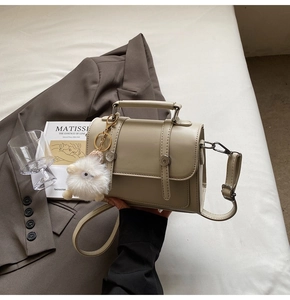 Detail view of a cream PU leather handbag with decorative straps and a plush sheep charm