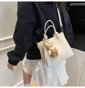 Detail of cream-colored pebble leather bucket bag with cute bear charm and ring handle