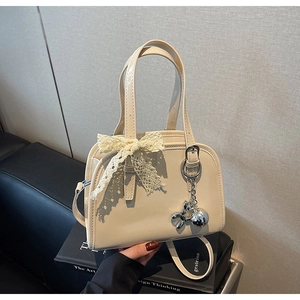 Close-up of cream patent leather Boston bag with lace bow and silver dog charm