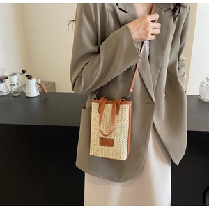 Straw woven crossbody bucket bag with brown faux leather trim shown in a cafe setting