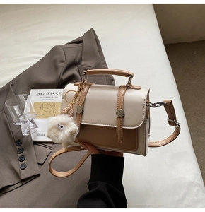 Detail view of cream and brown crossbody bag with plush sheep charm on soft bedding