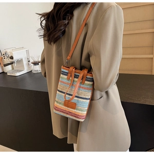 Detailed close-up of a colorful woven bucket bag with brown leather handles and strap