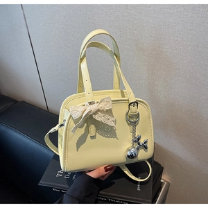 Detail of light yellow patent leather boston bag with lace bow and silver dog charm