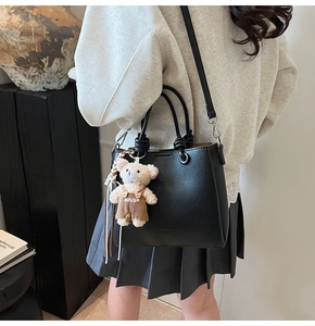 Detail of black lychee grain leather bucket bag with a cute plush bear pendant accessory